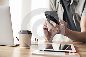 Closeup of young man hands with smart phone and laptop at home. Businessman working on computer in office