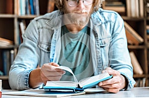 Closeup young man home library desk open read book turn page education concept
