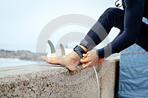 Closeup of young man putting on surfboard leash on beach. Guy wearing wetsuit and standing. Surfboarding safety concept.