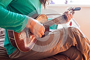 Closeup of a young man`s hands playing an acoustic guitar ukulele at the home. Man holding ukulele.