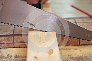 Closeup of a young man sawing a wooden board with a handsaw