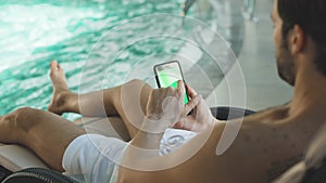 Closeup young man scrolling mobile phone poolside. Man hands holding smartphone
