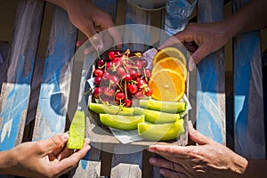 Closeup of young and old hands from grandmother and teenager nephew eating some fresh season fruits on the wood table. healhty