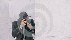 Closeup of young paparazzi man in hat photographing celebrities on camera while spy behind the wall