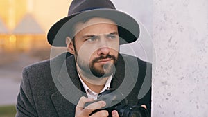 Closeup of young paparazzi man in hat photographing celebrities on camera while spy behind the wall