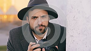 Closeup of young paparazzi man in hat photographing celebrities on camera while spy behind the wall