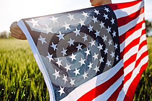 Closeup of a young patriotic farmer stands among new harvest. Boy walking with the american flag on the green wheat