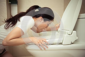 Closeup of young pretty woman vomiting into toilet