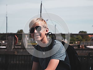 Closeup of young Scandinavian boy with pilot sunglasses sitting and smiling in old port