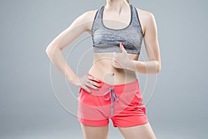 Closeup of young slim woman show thumbs up with six-pack torso  on white background