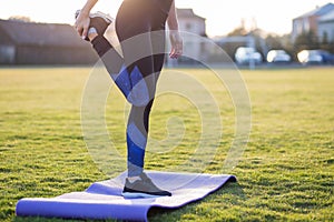 Closeup of young sportive woman doing exercise before running in morning field outdoors