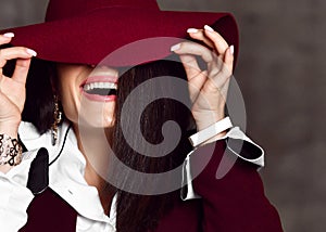 Closeup of young stylish woman brunette in black jacket and white shirt pulls down hat brim hiding her eyes and laughs