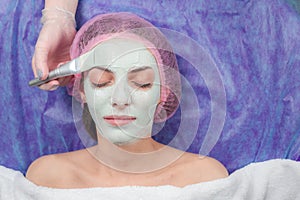 Closeup Young woman with clay facial mask at beauty salon