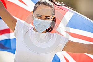 Closeup of a young woman in disposable face mask with a UK flag behind her