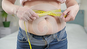 Closeup of young woman with fat belly measuring her waistline.