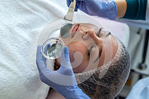 Closeup of young woman getting hydrating procedure facial spa massage by dermatologist in clinic