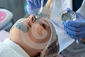 Closeup of young woman getting hydrating procedure facial spa massage by dermatologist in clinic