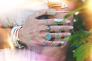 closeup of young woman hand and arm with lot of boho style jewrly, rings and bracelets outdoor light leak