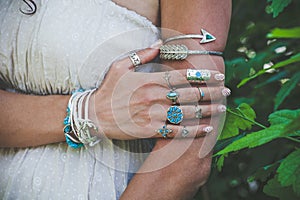 closeup of young woman hand and arm with lot of boho style jewrly, rings and bracelets outdoor shot