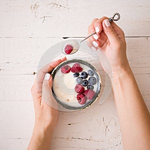 Closeup of Young woman hands with a bowl of yogurt. Girl eating organic yogurt for breakfast with fresh berries