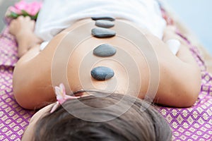 Closeup on young woman having hot stone massage on back in spa