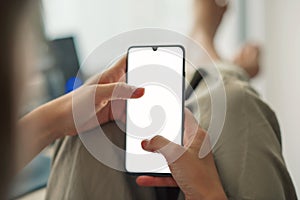 Closeup of a young woman holding a mobile phone with blank white screen sitting at home during the lockdown. Mockup image of a