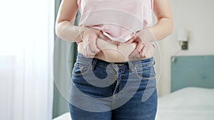 CLoseup of young woman in jeans holding fat fold on her belly. Concept of excessive weight, obese female, dieting and