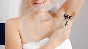 Closeup of young woman with long armpit hair shaving with razor in bathroom. Concept of hygiene, natural beauty, feminity and body