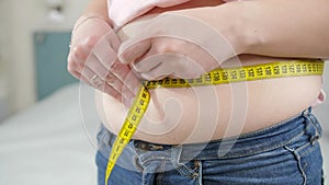 Closeup of young woman loosing weight measuring her waist. Concept of dieting, unhealthy lifestyle, overweight and