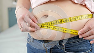 Closeup of young woman loosing weight measuring her waist. Concept of dieting, unhealthy lifestyle, overweight and