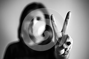 Closeup of a young woman shows victory sign with her hand. Dramatic black and white closeup of a girl being protected with medical