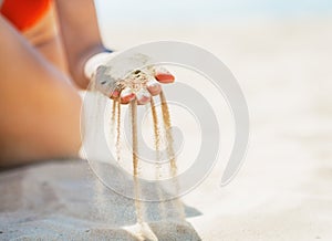 Closeup on young woman sitting on beach and playing with sand