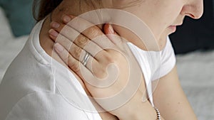 Closeup of young woman sitting on bed and rubbing her aching neck in morning. Concept of healthcare problems, pain relief and
