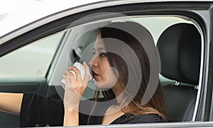 Closeup young woman sitting in car holding coffee cup and drinking, as seen from outside drivers window, female driver