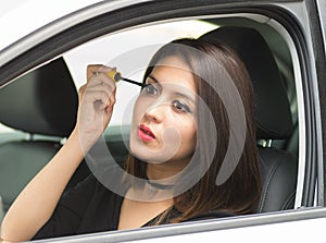 Closeup young woman sitting in car putting on makeup looking in mirror, as seen from outside drivers window, female