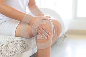 Closeup young woman sitting on sofa and feeling knee pain