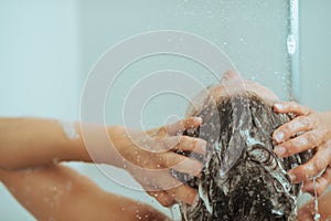 Closeup on young woman washing head with shampoo