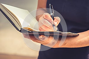 Closeup of young woman writing down letters in notepad for making note at her diary with her hand. Business and Lifestyle concept