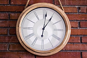 Closeâ€“up of a wooden wall clock with roman numerals hanging in a red brick wall.