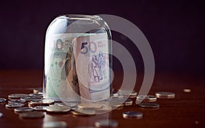 Closing glass cup on Colombia Peso banknotes on a wooden table with coins with