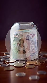 Closing glass cup on Colombia Peso currency cash on a wooden table with coins, with dark background