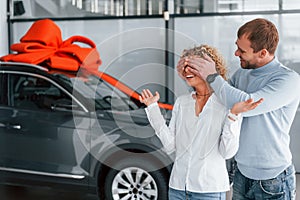 Closing her eyes by hands. Husband makes gift for his wife. Modern new car