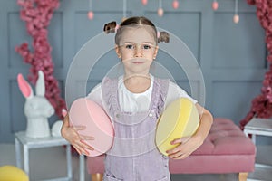 Closup portrait smiling Young girl with hairstyle buns. Beautiful little girl with big eyes playing with Easter eggs. Family holid