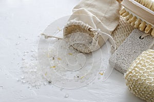 Cloth bag of sea salt,sponges, pumice for feet on the white surafce.Table at the spa salon and body care accessories on it