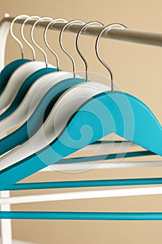 Clothes hangers on metal rail against beige background, closeup view