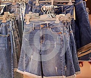 Clothes on hangers in store. Womens denim blue shorts hang on clothing rack. Shopping time concept