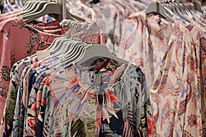 Clothes on hangers in store. Womens floral blouses hang on clothing rack. Shopping time concept
