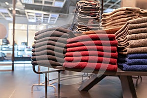 Clothes are neatly stacked on the shelves in the store. pullovers, sweaters warm of different colors are plain. red and photo