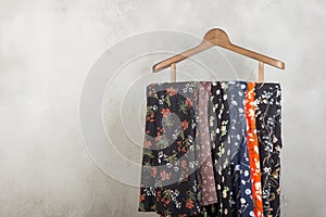 clothes rack with trendy dresses in floral print on wooden floor and grey concrete background