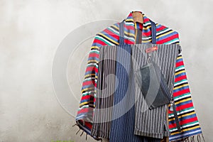 Clothes rack with trendy striped pants and plaid, shoes, bag on grey concrete background